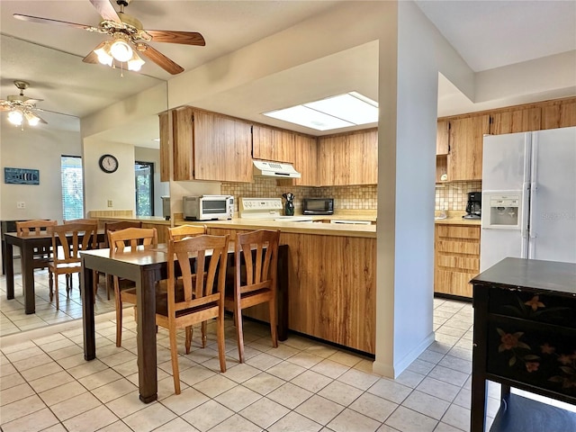 kitchen with white refrigerator with ice dispenser, kitchen peninsula, decorative backsplash, light tile patterned floors, and range