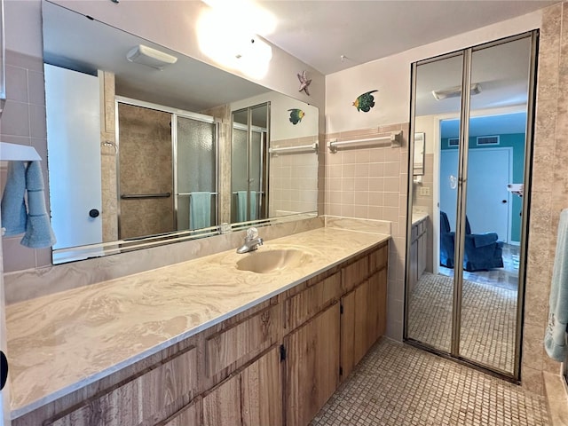 bathroom with tile patterned floors, a shower with door, vanity, and tile walls