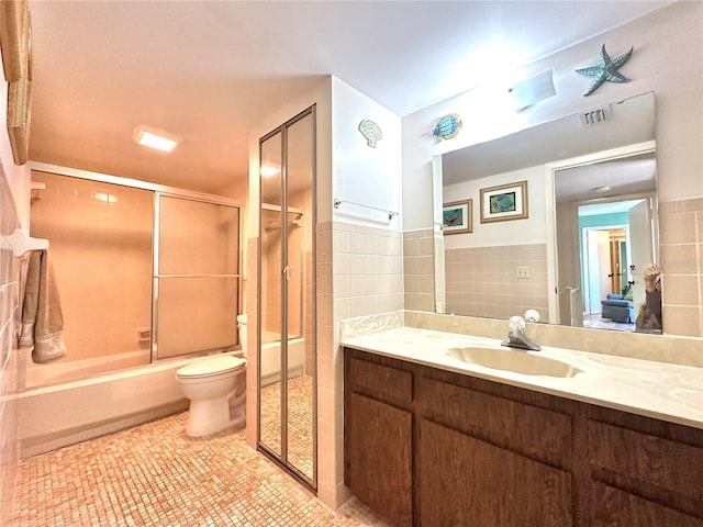 full bathroom featuring tile patterned floors, bath / shower combo with glass door, vanity, tile walls, and toilet