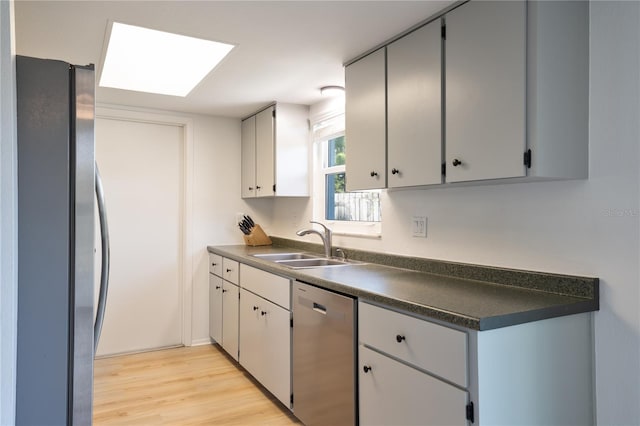 kitchen with appliances with stainless steel finishes, sink, light wood-type flooring, and a skylight