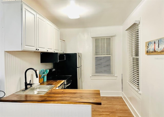 kitchen with white cabinets, butcher block countertops, light hardwood / wood-style flooring, and sink