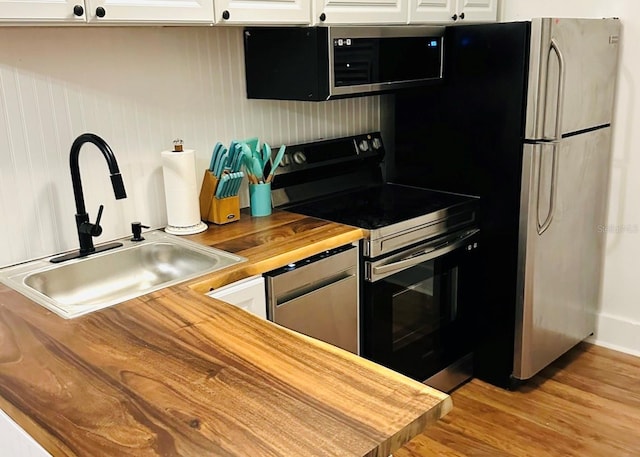 kitchen featuring butcher block countertops, white cabinetry, stainless steel appliances, and sink