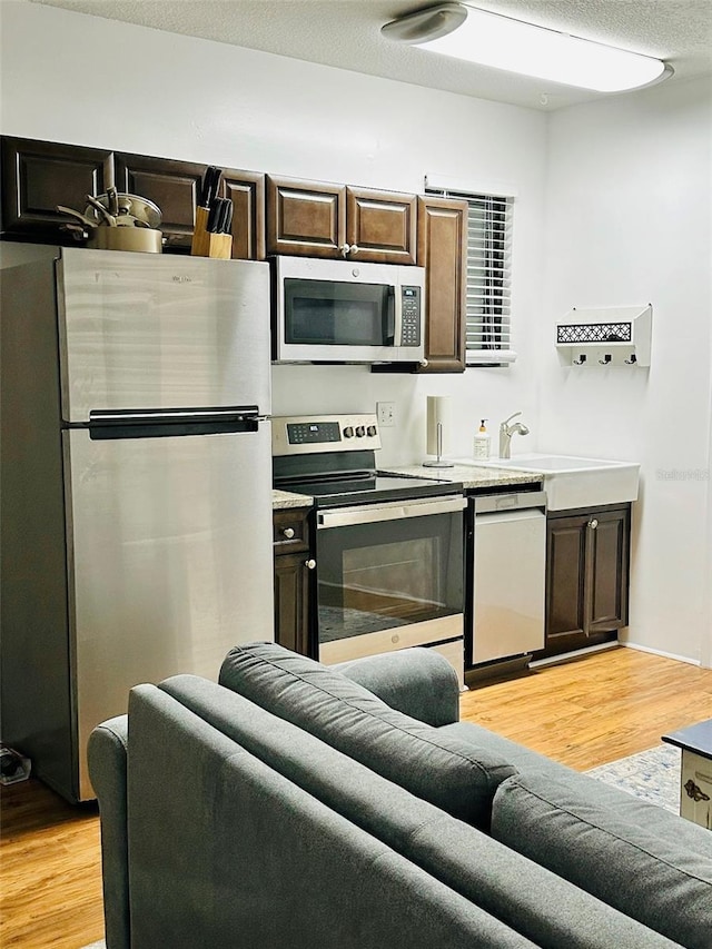 kitchen featuring appliances with stainless steel finishes, a textured ceiling, light hardwood / wood-style floors, and dark brown cabinetry