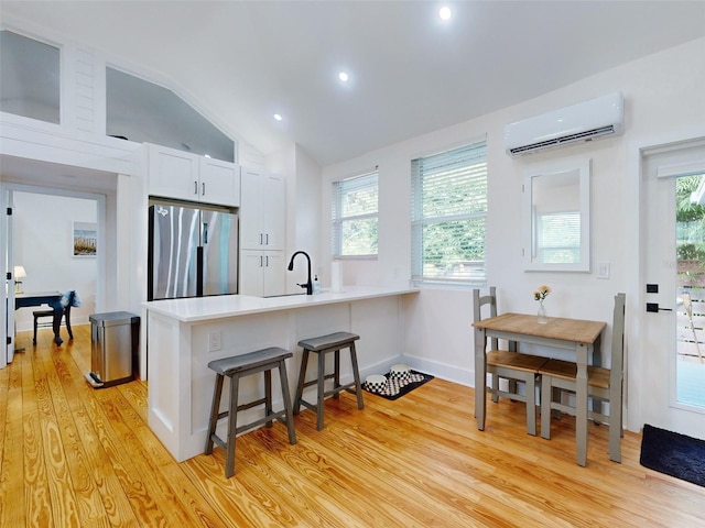 kitchen with a wall unit AC, stainless steel fridge, a healthy amount of sunlight, and vaulted ceiling