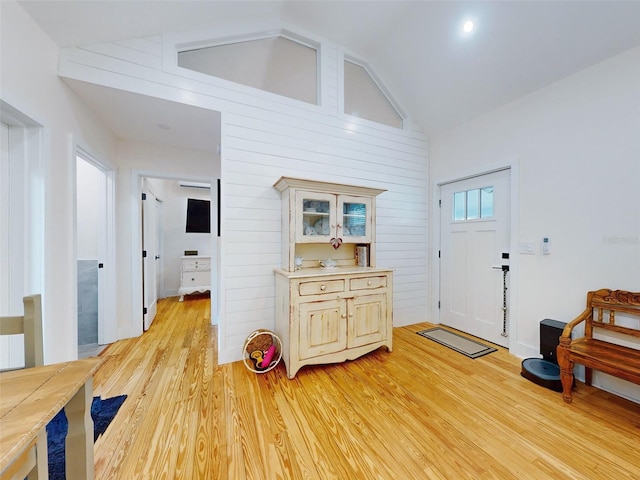 foyer with light wood-type flooring, high vaulted ceiling, and wood walls