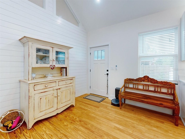 foyer entrance with light wood-type flooring, wooden walls, and vaulted ceiling