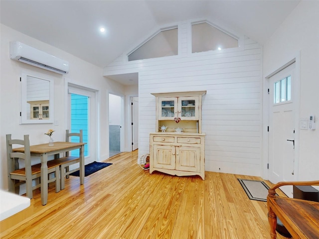 interior space with light wood-type flooring, wooden walls, vaulted ceiling, and an AC wall unit