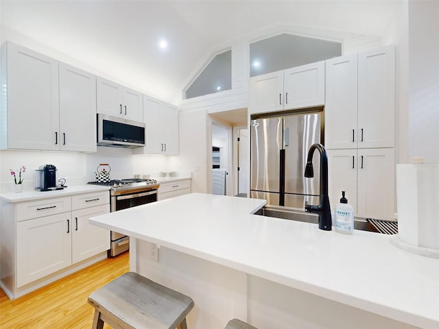 kitchen with a kitchen bar, white cabinets, stainless steel appliances, and vaulted ceiling