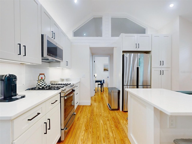 kitchen with white cabinets, vaulted ceiling, stainless steel appliances, and light hardwood / wood-style flooring