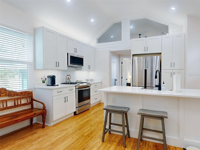 kitchen featuring stainless steel appliances, lofted ceiling, a breakfast bar area, white cabinets, and light wood-type flooring