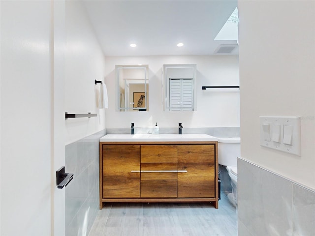 bathroom with wood-type flooring, vanity, toilet, and tile walls