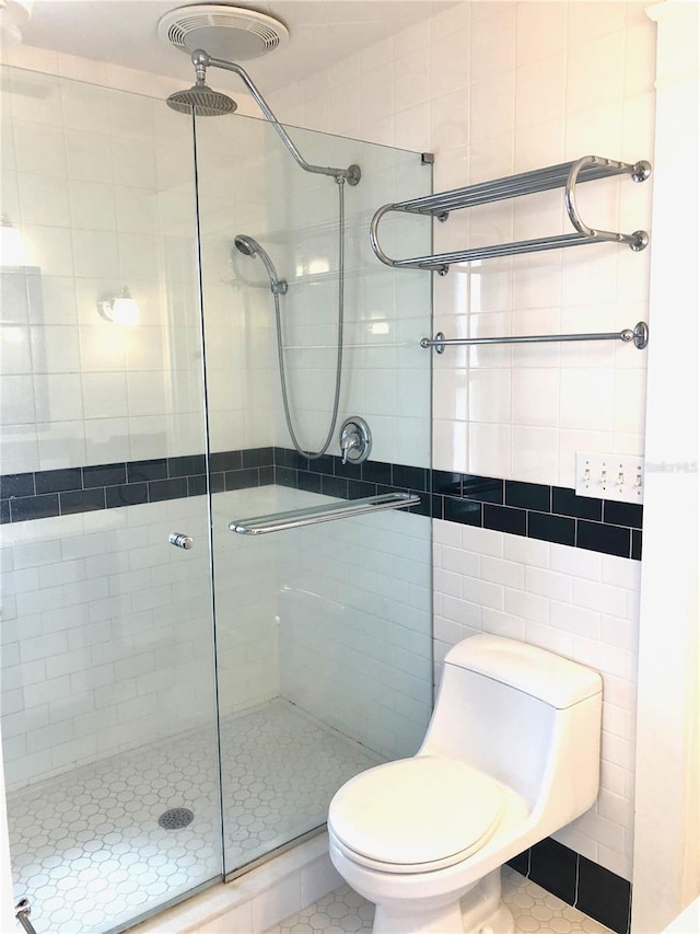 bathroom featuring toilet, a shower with door, tile patterned floors, and tile walls