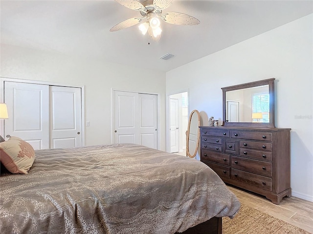 bedroom with multiple closets, visible vents, light wood finished floors, and a ceiling fan