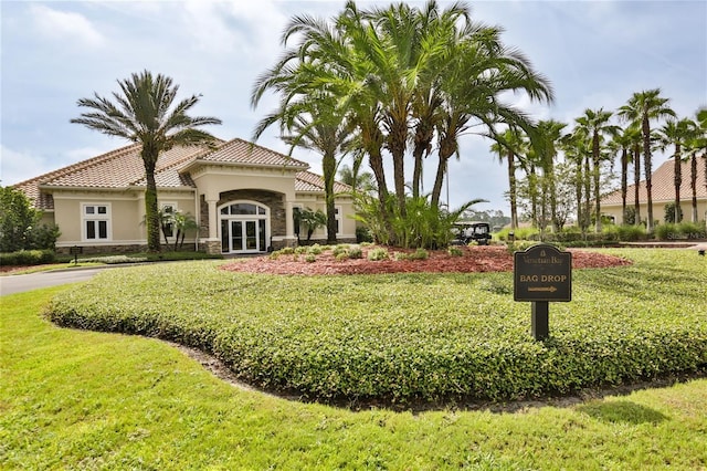 view of front facade with stone siding, a tiled roof, french doors, a front yard, and stucco siding