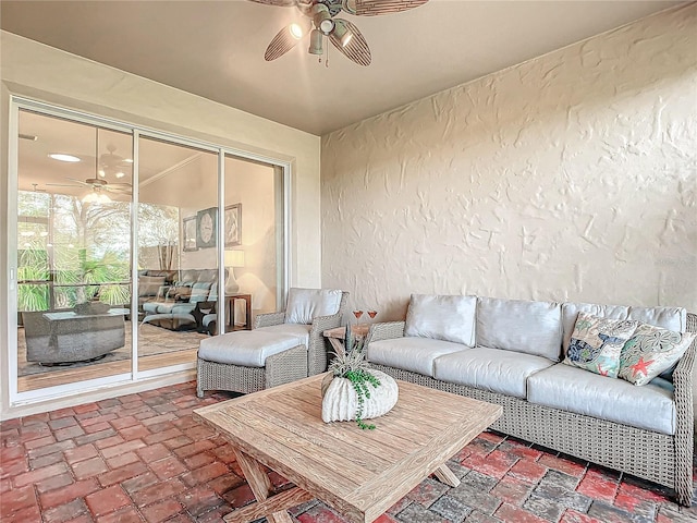 living area with ceiling fan, a textured wall, and brick floor