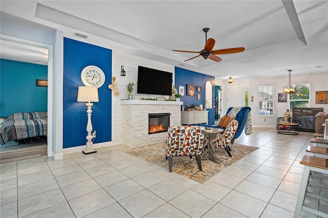 tiled living room with a raised ceiling, ceiling fan, and a fireplace