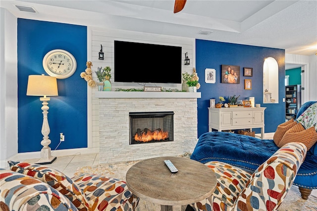 living room with ceiling fan, a stone fireplace, and light tile patterned floors