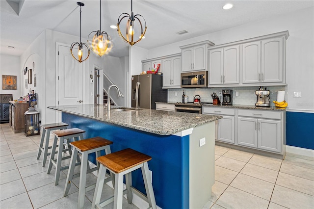 kitchen featuring appliances with stainless steel finishes, tasteful backsplash, dark stone counters, a center island with sink, and a breakfast bar area