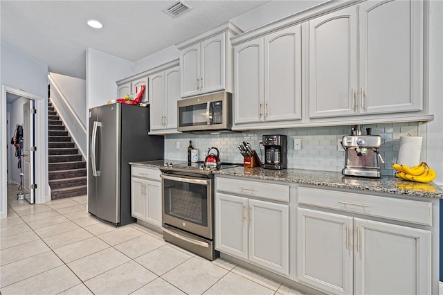 kitchen featuring backsplash, light tile patterned floors, stainless steel appliances, and dark stone counters