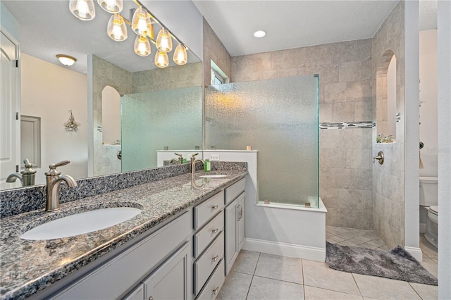 bathroom with vanity, tile patterned flooring, toilet, tiled shower, and a textured ceiling