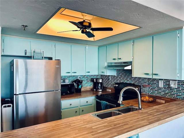 kitchen with wooden counters, range, decorative backsplash, and stainless steel refrigerator