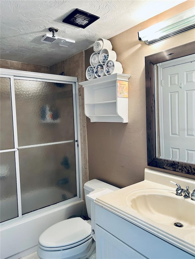 full bathroom featuring vanity, an AC wall unit, bath / shower combo with glass door, toilet, and a textured ceiling