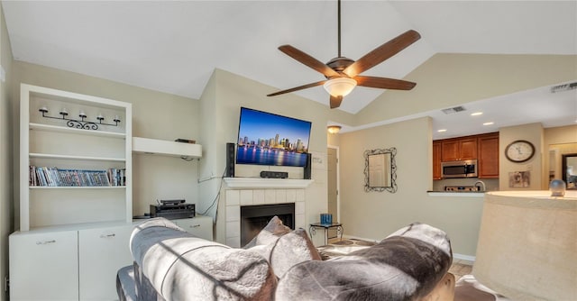 living room featuring a tiled fireplace, ceiling fan, built in shelves, and vaulted ceiling