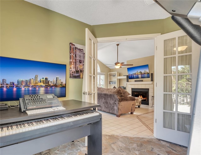 misc room featuring ceiling fan, french doors, a textured ceiling, lofted ceiling, and a tiled fireplace