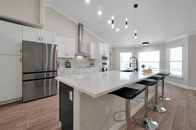 kitchen featuring wall chimney exhaust hood, stainless steel appliances, a kitchen island with sink, sink, and lofted ceiling