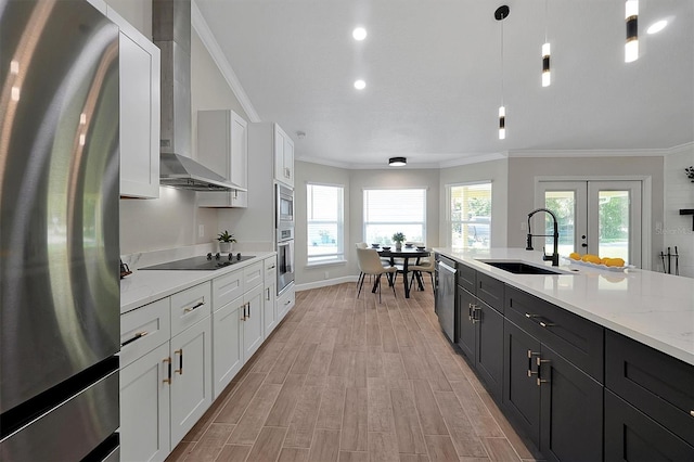 kitchen with white cabinetry, sink, wall chimney exhaust hood, hanging light fixtures, and appliances with stainless steel finishes