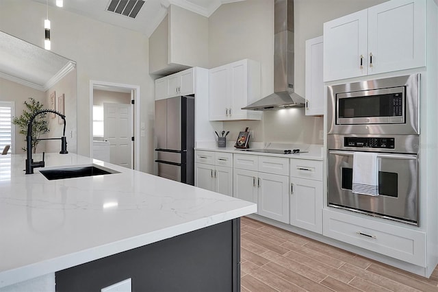 kitchen with white cabinetry, sink, wall chimney exhaust hood, light hardwood / wood-style floors, and appliances with stainless steel finishes