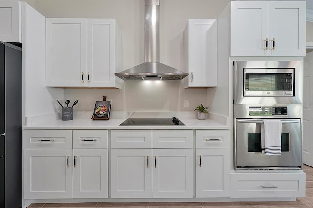 kitchen with light stone countertops, wall chimney exhaust hood, stainless steel appliances, white cabinets, and light hardwood / wood-style floors