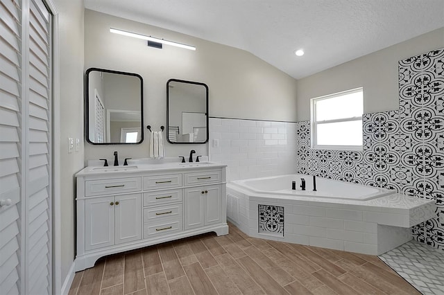 bathroom featuring tiled bath, a textured ceiling, vaulted ceiling, vanity, and hardwood / wood-style flooring