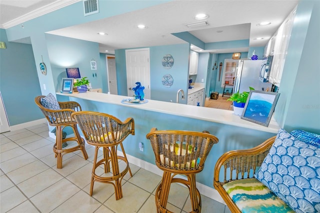 kitchen featuring kitchen peninsula, light tile patterned floors, white cabinetry, fridge, and a breakfast bar area