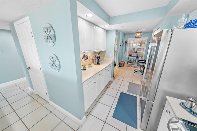 kitchen with white cabinets, stainless steel fridge, light tile patterned floors, and backsplash