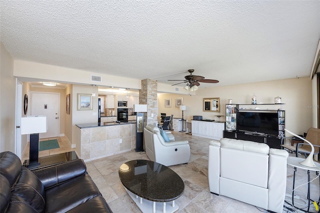 living room featuring ceiling fan, ornate columns, and a textured ceiling