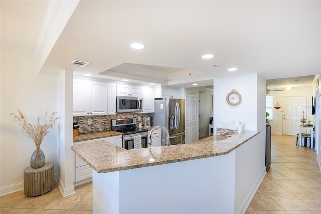 kitchen with white cabinets, appliances with stainless steel finishes, tasteful backsplash, light stone counters, and kitchen peninsula