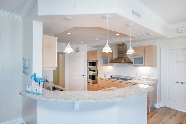 kitchen featuring wall chimney exhaust hood, stainless steel appliances, kitchen peninsula, decorative light fixtures, and light brown cabinetry