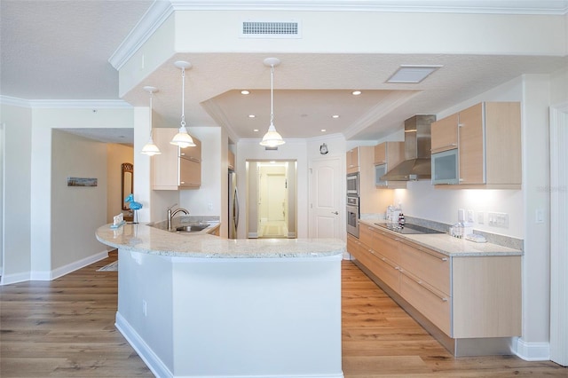 kitchen featuring kitchen peninsula, light brown cabinets, pendant lighting, and wall chimney range hood