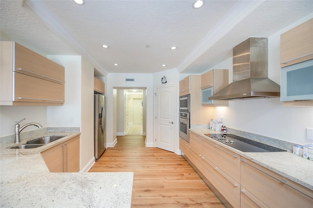 kitchen with sink, stainless steel appliances, wall chimney range hood, light hardwood / wood-style flooring, and a textured ceiling