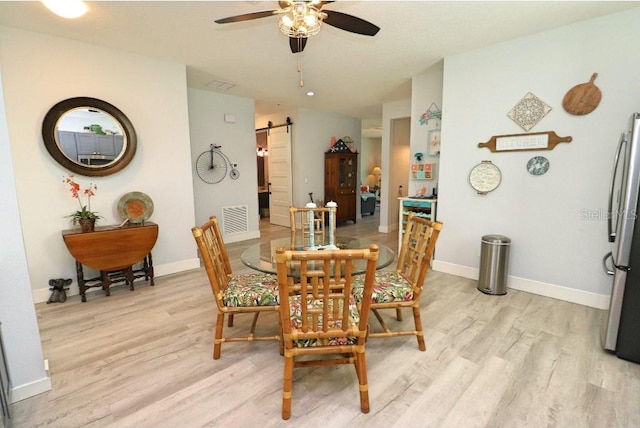 dining space featuring ceiling fan, a barn door, and light hardwood / wood-style floors