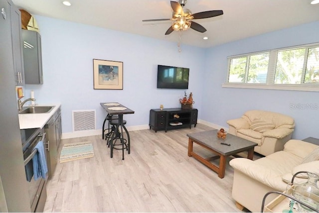 living room featuring ceiling fan, light wood-type flooring, and sink