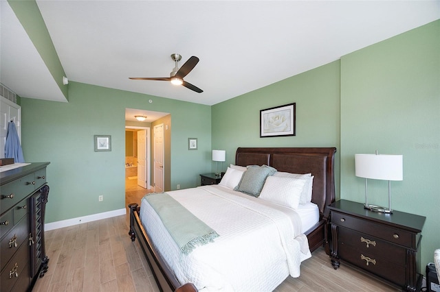 bedroom with light wood-type flooring, ceiling fan, and connected bathroom