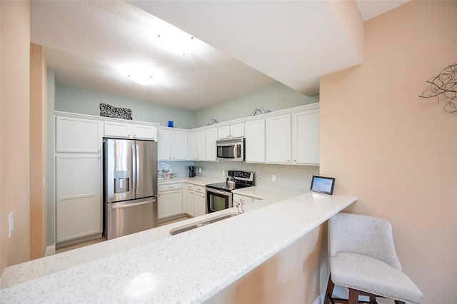 kitchen with a kitchen bar, appliances with stainless steel finishes, decorative backsplash, kitchen peninsula, and white cabinets