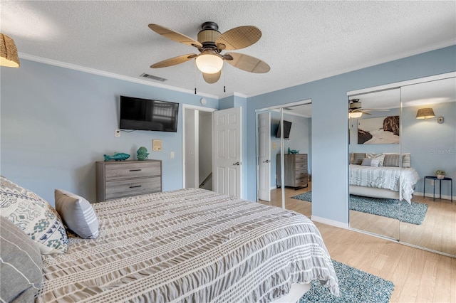 bedroom with a textured ceiling, light hardwood / wood-style floors, ceiling fan, and multiple closets