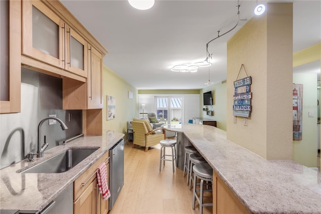 kitchen with dishwasher, sink, light stone counters, a breakfast bar, and light wood-type flooring