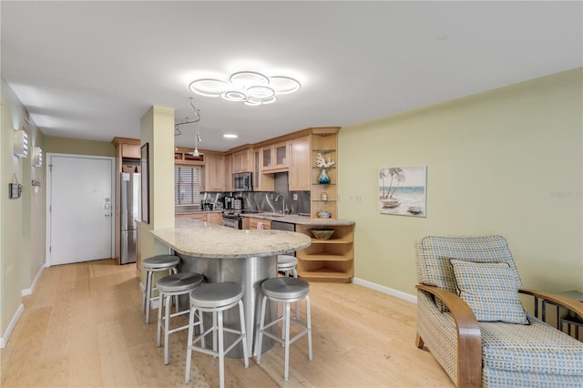 kitchen featuring kitchen peninsula, light wood-type flooring, stainless steel appliances, and tasteful backsplash