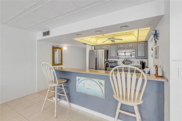 kitchen with gray cabinetry, appliances with stainless steel finishes, light tile patterned flooring, a kitchen bar, and kitchen peninsula