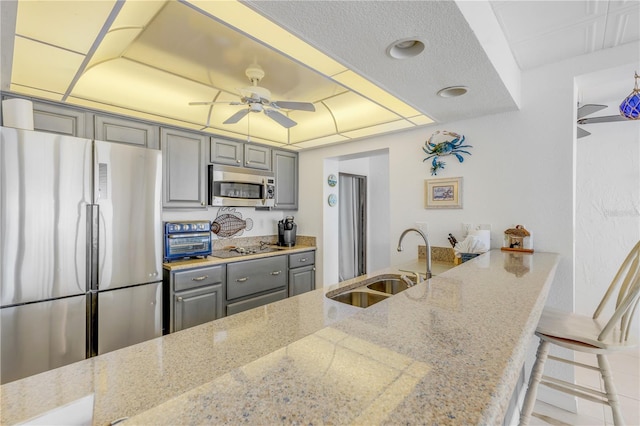 kitchen with kitchen peninsula, light stone counters, sink, and appliances with stainless steel finishes