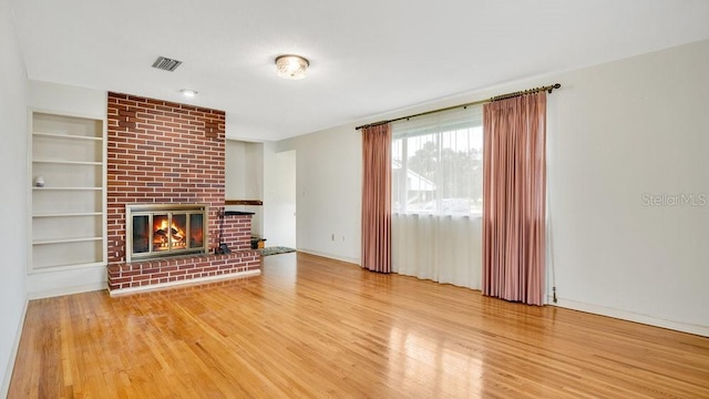 unfurnished living room featuring a brick fireplace, hardwood / wood-style flooring, and built in shelves